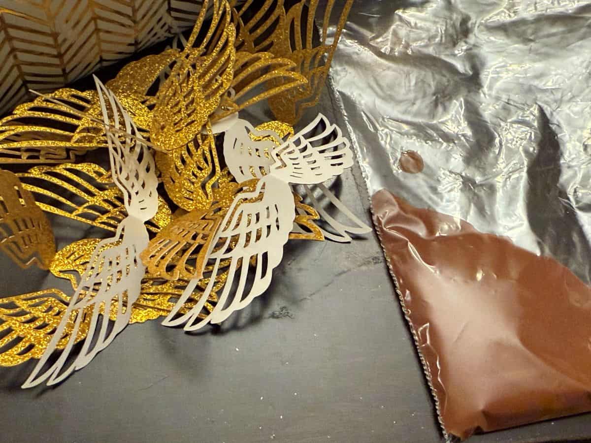 melted chocolate in a sandwich bag next to a pile of folded gold glitter cardstock wings