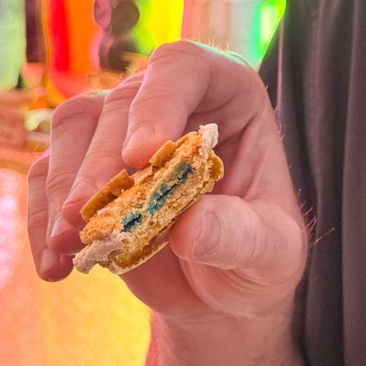 a Sorting Hat Butterbeer Macaron bitten in half and held in a hand to show a blue interior