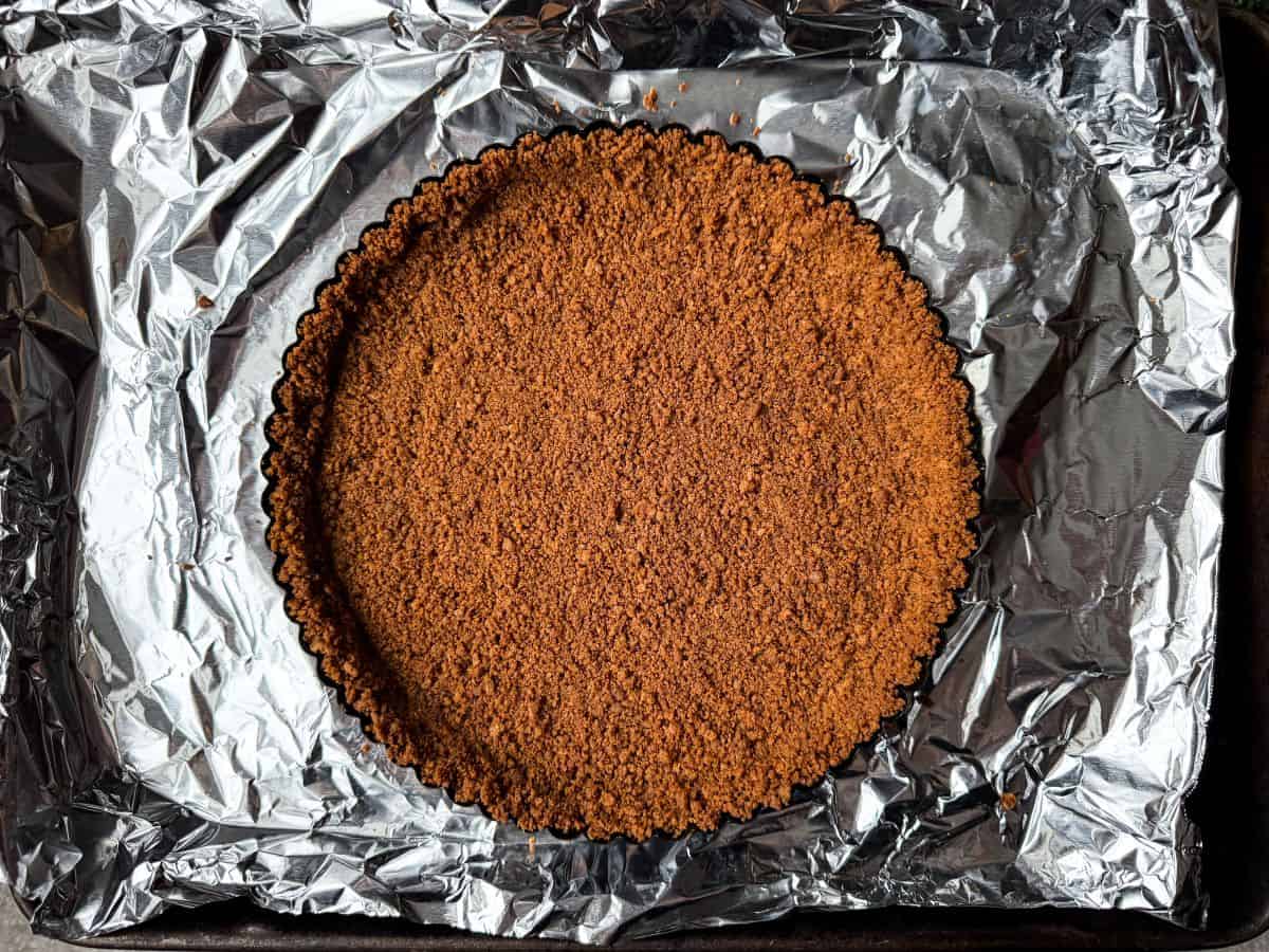 a gingersnap cookie crust pressed into a tart pan on a foil lined baking sheet after baking