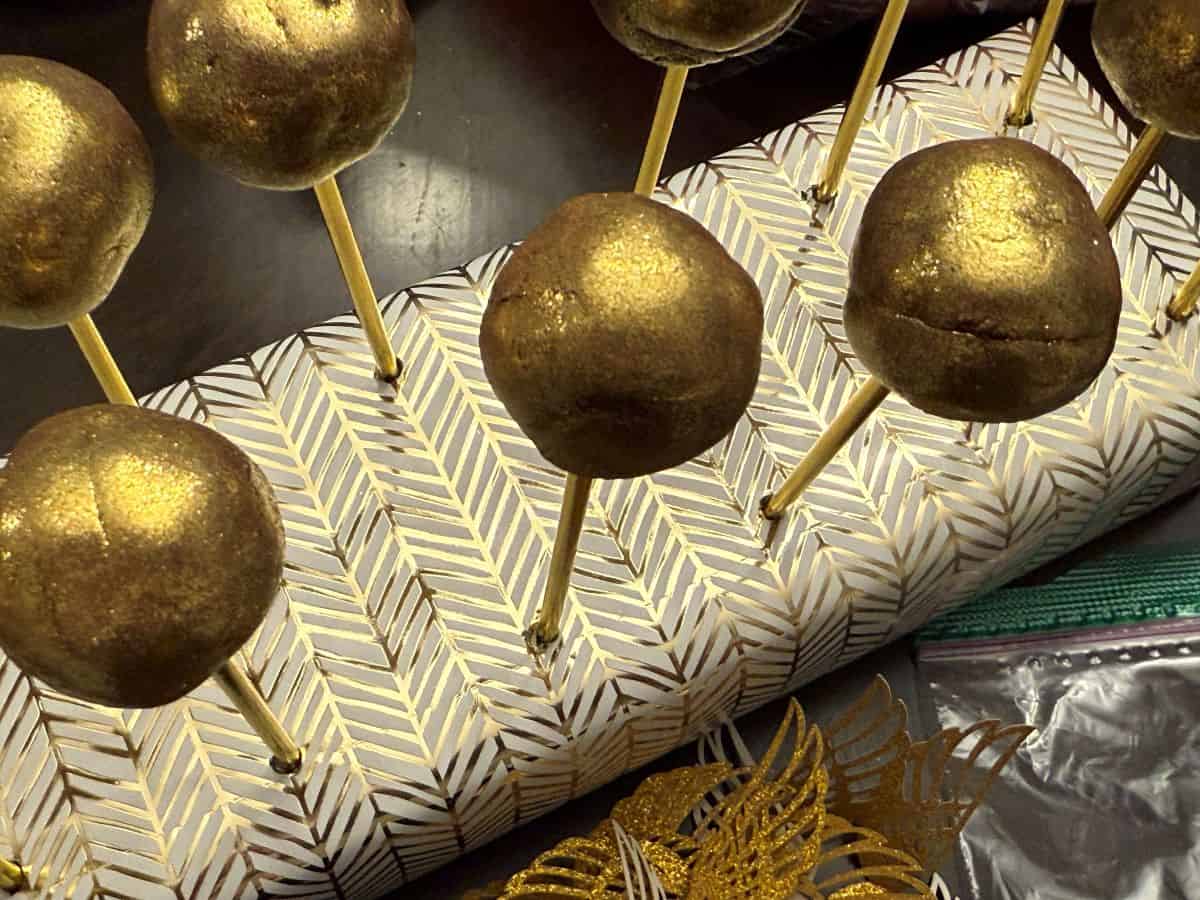 gold brigadeiro candies on gold sticks in a gold patterned display block