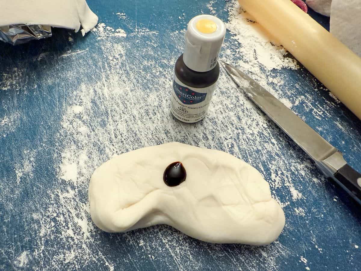 white fondant on a powdered sugar dusted cutting mat with a blob of gold food coloring gel on top