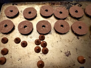 fudge stripe cookies upside down on a baking sheet next to unwrapped Hershey's Kisses candies