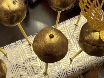 a dot of melted chocolate on top of a gold brigadeiro candy on a gold stick