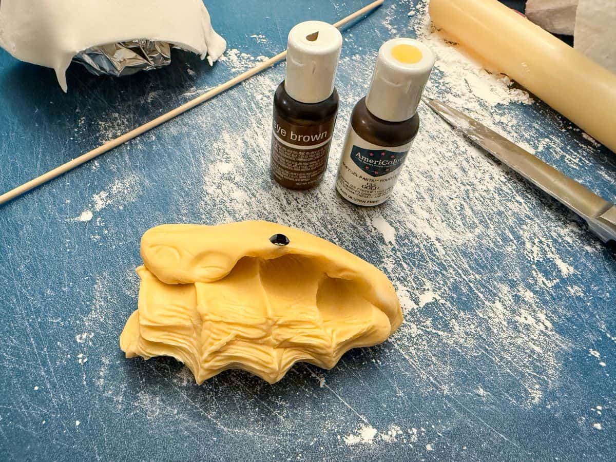 gold tinted fondant next to bottles of brown and gold food coloring gel on a cutting mat