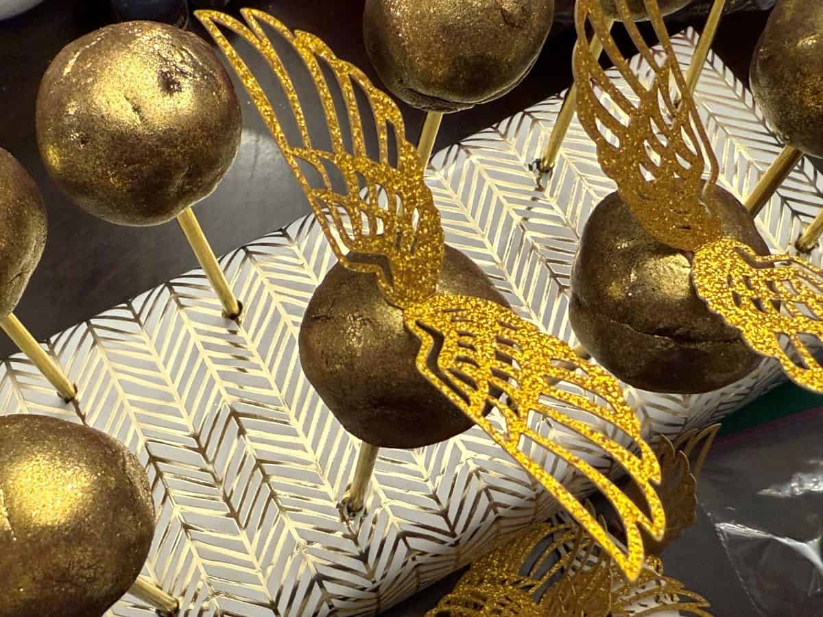 gold wings attached to the top of golden brigadeiro candies on sticks