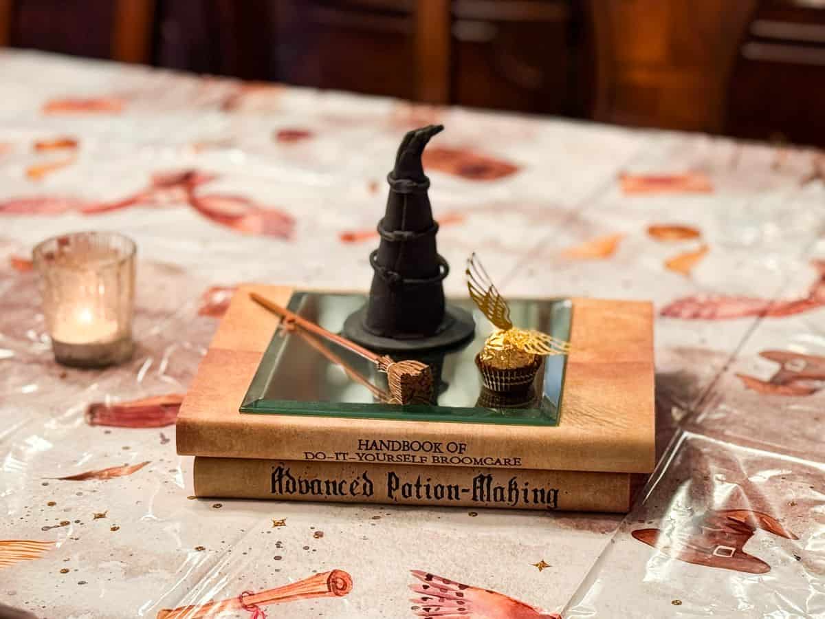 Harry Potter spell books stacked on a dining room table with a wizard hat, miniature broom, and Golden Snitch Candy