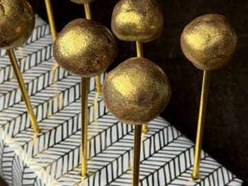 golden brigadeiro candies on gold sticks in a styrofoam block