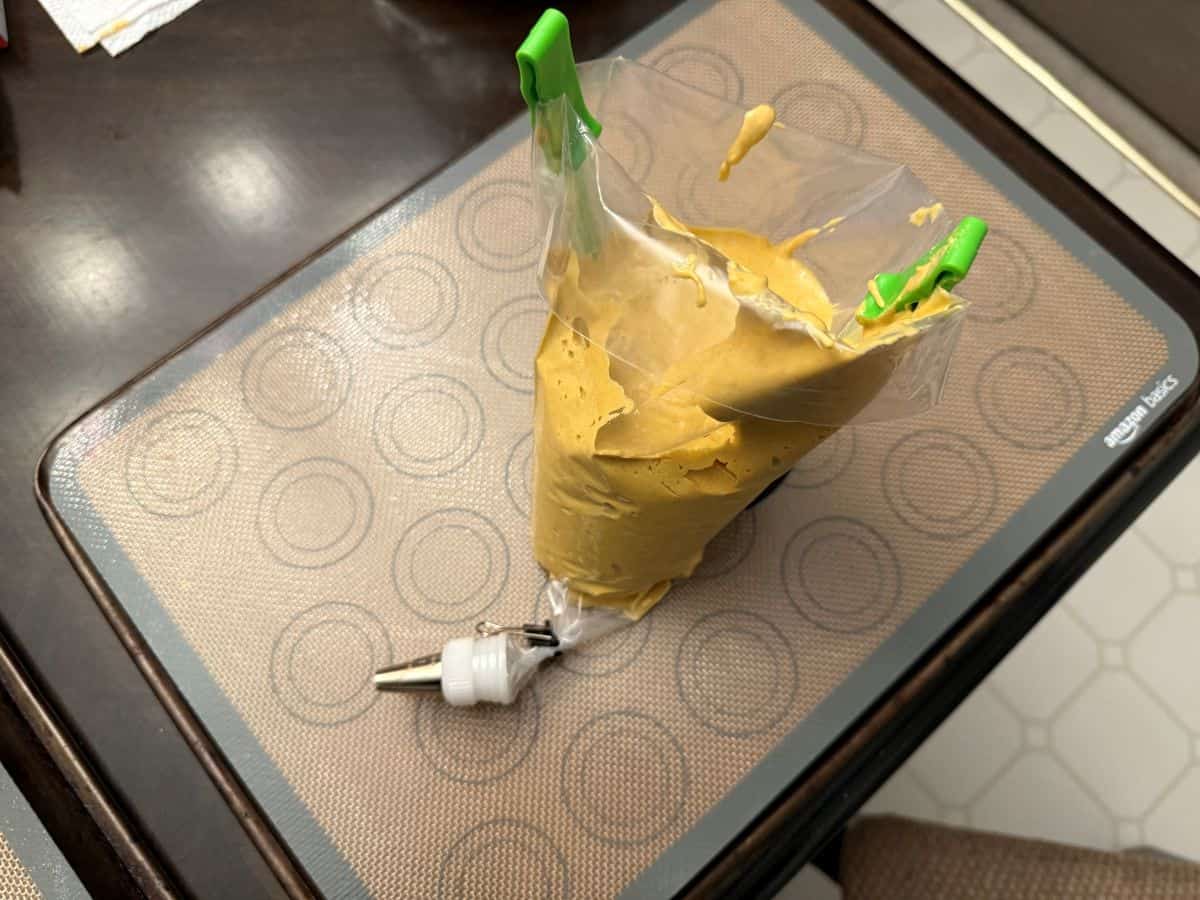 gold colored macaron batter in a piping bag held upright in a piping bag holder