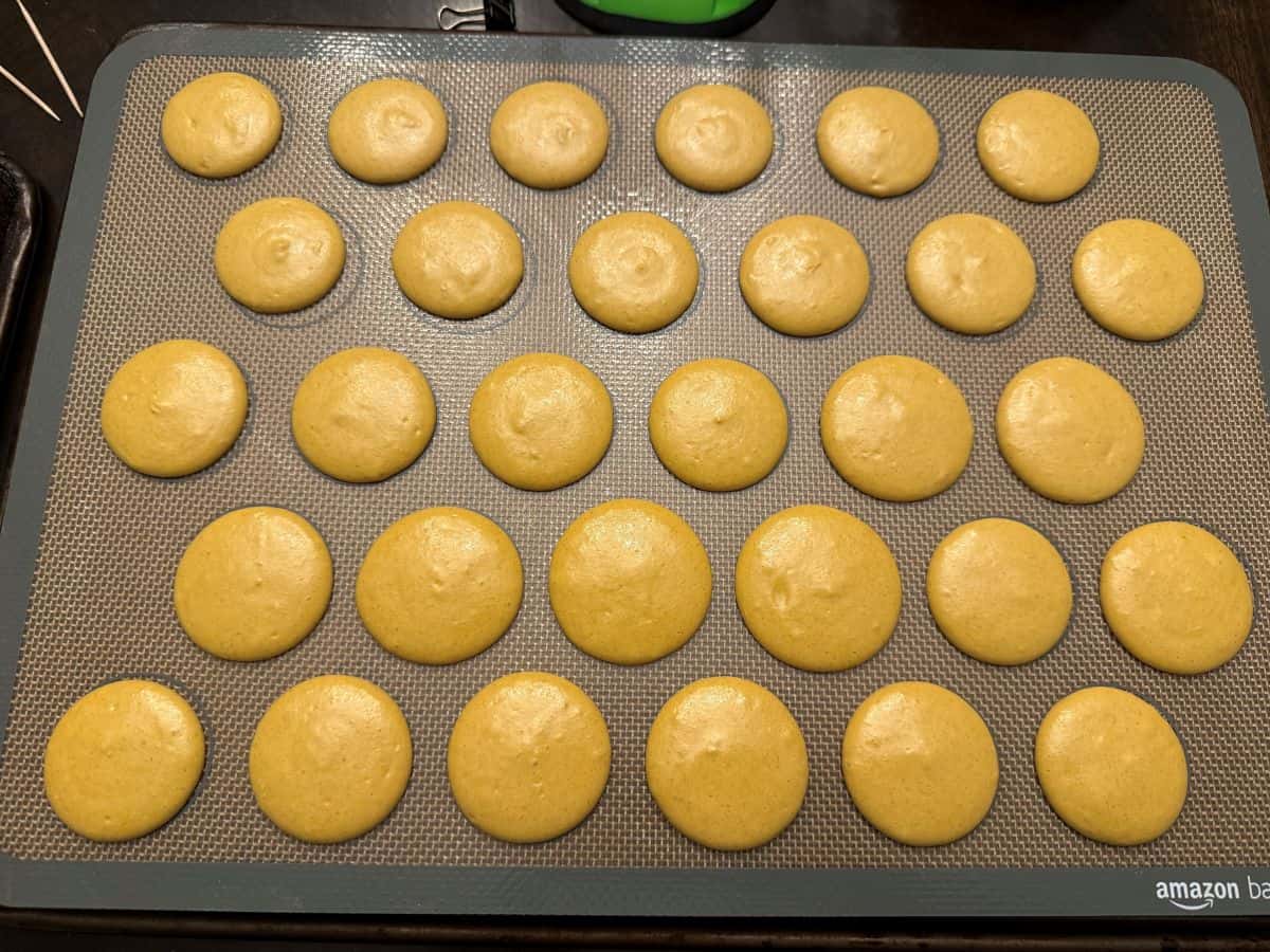 macaron batter piped into 1-inch circles on a macaron mat