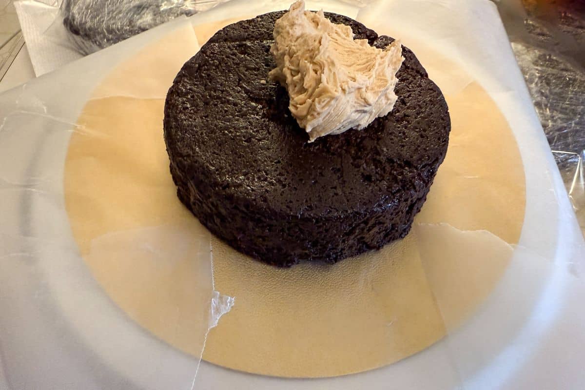 a single chocolate cake layer on top of pieces of waxed paper with a mound of butterscotch buttercream on top of the cake