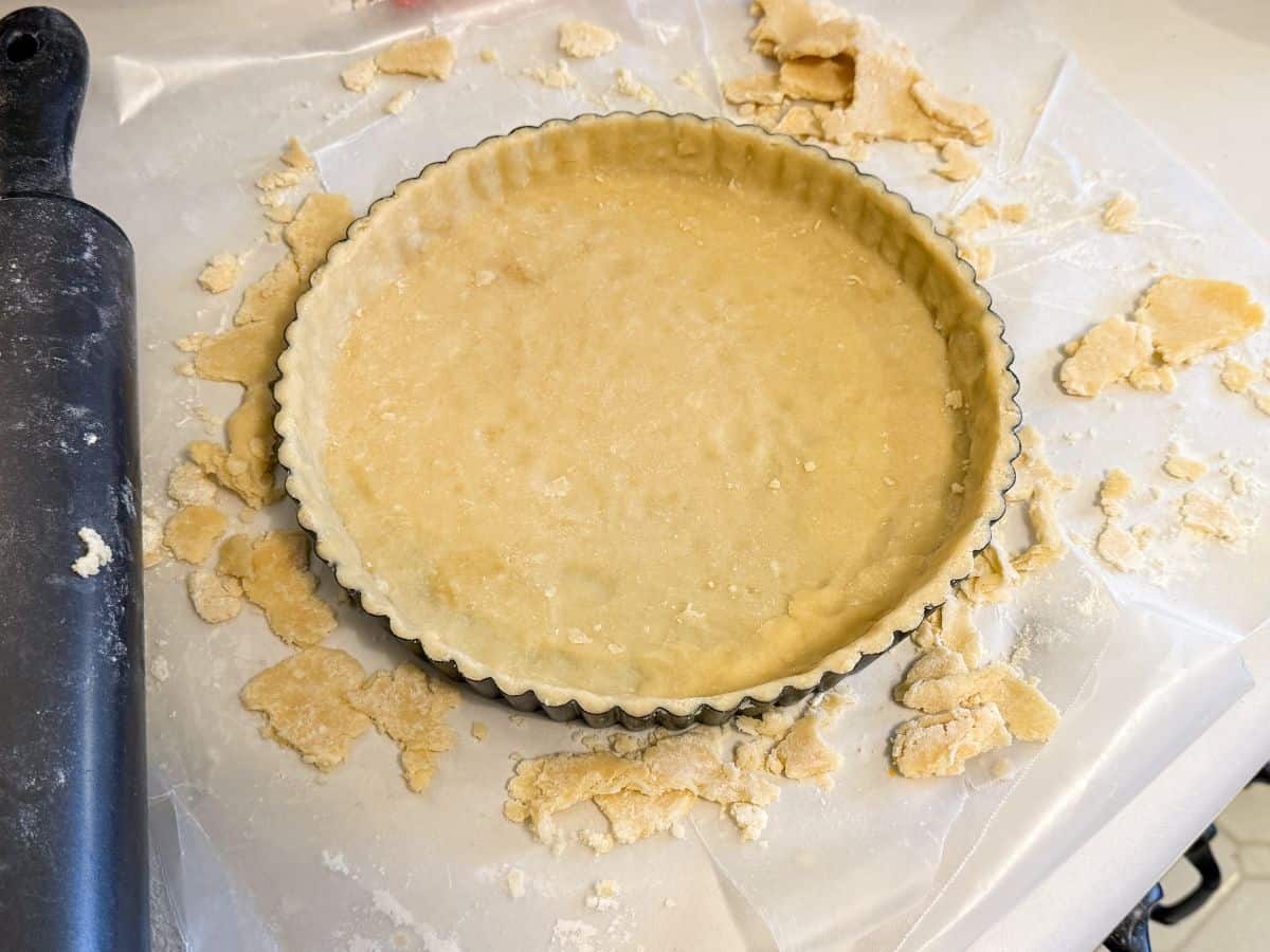 tart dough fitted into a tart pan with a neat top edge and the overhang pieces on the waxed paper below