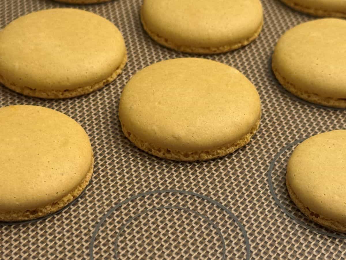 gold tinted macaron shells cooling on a macaron mat