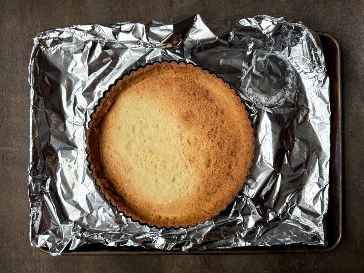 a baked cookie tart shell on a foil lined baking sheet