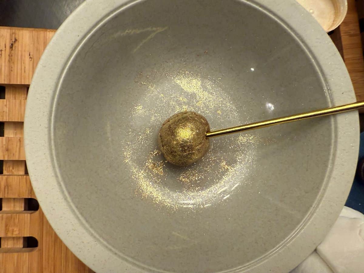 a golden candy stick inserted into a gold ball of brigadeiro candy in a bowl