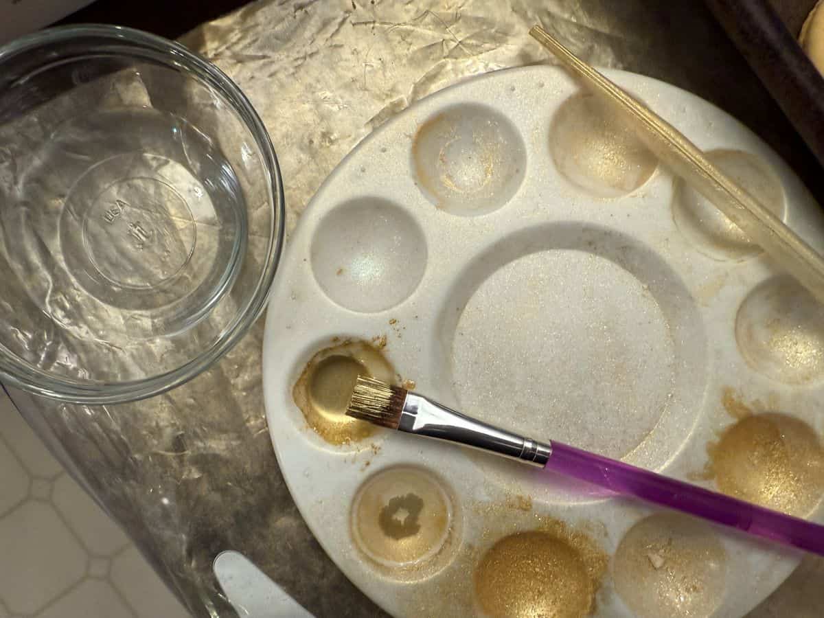edible gold luster dust suspension in the well of a paint palette with a food grade paintbrush in it