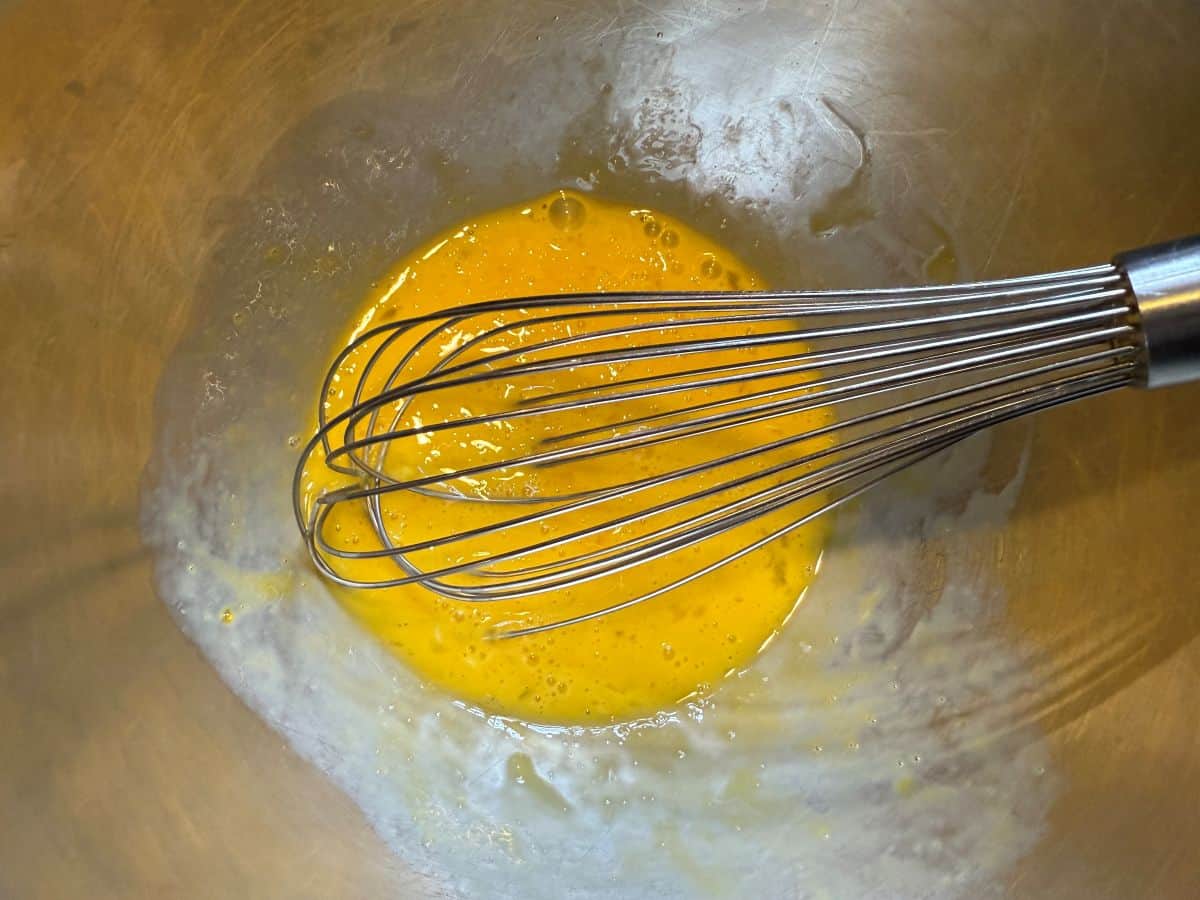 eggs and yolks whisked together in a bowl with a wire whisk