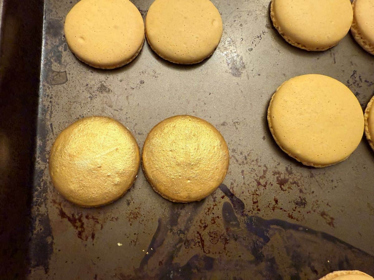 gold painted macaron shells paired up on a baking sheet