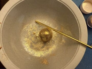 a gold ball of fudge in a bowl next to a gold candy stick