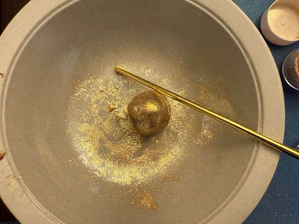 a gold ball of fudge in a bowl next to a gold candy stick