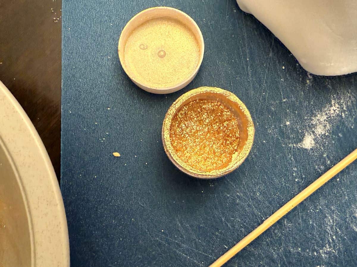 edible gold glitter in a container on top of a cutting mat