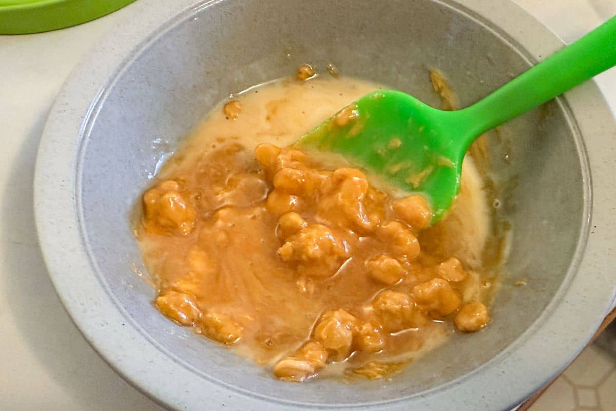 butterscotch chips starting to melt with heavy cream in a bowl and a green silicone spatula