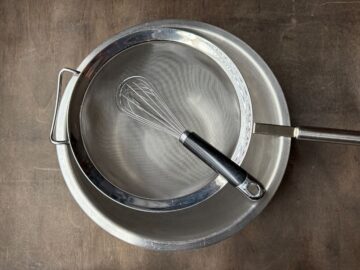 a fine mesh sieve set over a metal bowl with a wire whisk in the bowl