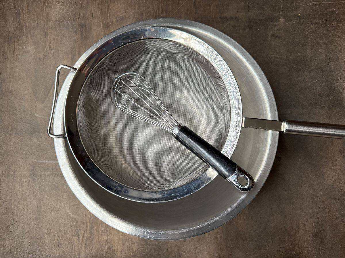 a fine mesh sieve set over a metal bowl with a wire whisk in the bowl