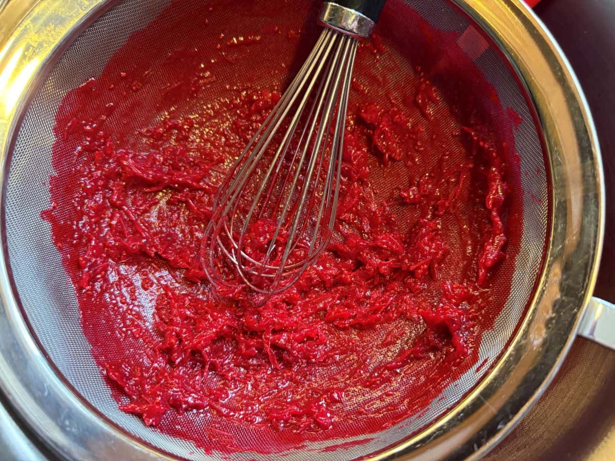 cranberry pulp left behind in a fine mesh strainer after being whisked into the bowl beneath