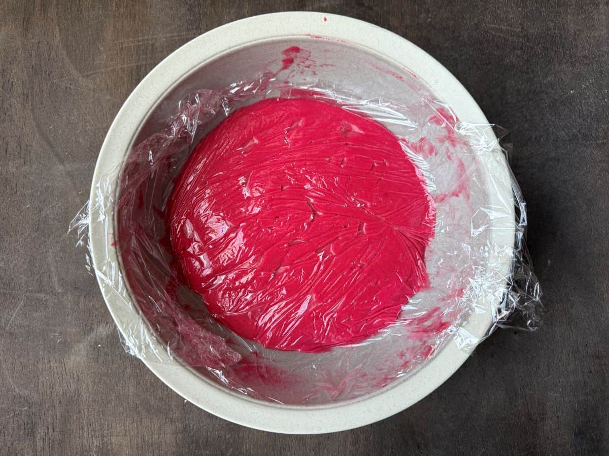 plastic wrap pressed on the surface of cranberry curd in a bowl