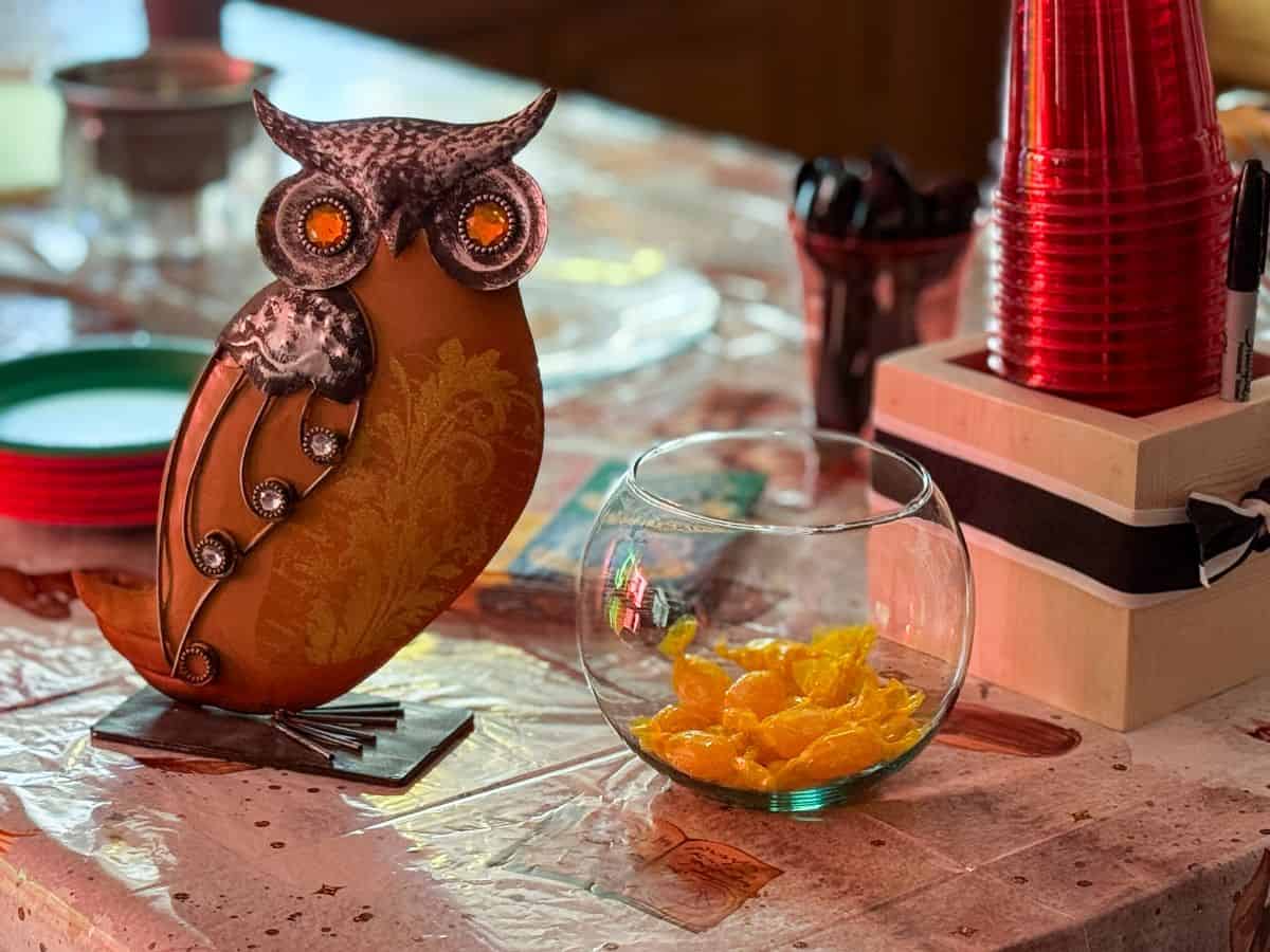 a metal owl next to a round glass bowl filled with yellow hard candies