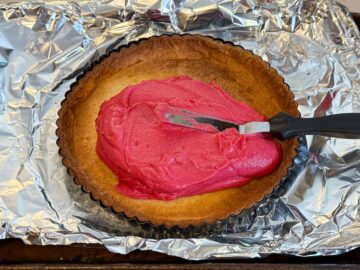 cranberry curd being spread with a small offset spatula into a cookie tart shell crust