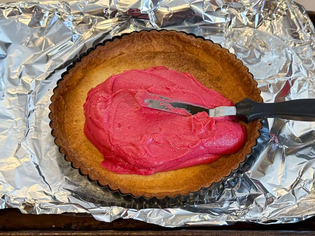 cranberry curd being spread with a small offset spatula into a cookie tart shell crust
