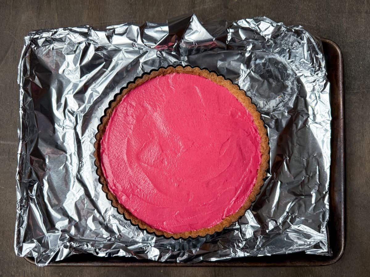 an overhead photo of a filled cranberry curd tart on an aluminum foil lined baking sheet