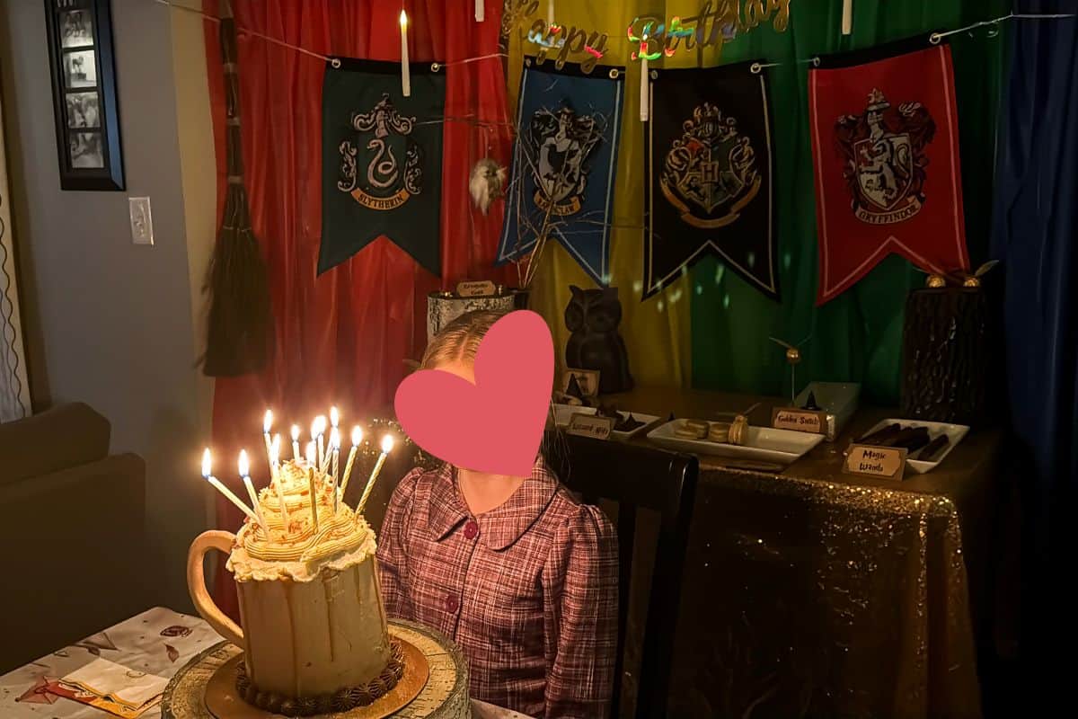 a girl dressed as Luna Lovegood from Harry Potter in front of a Butterbeer Cake with long candles in the top