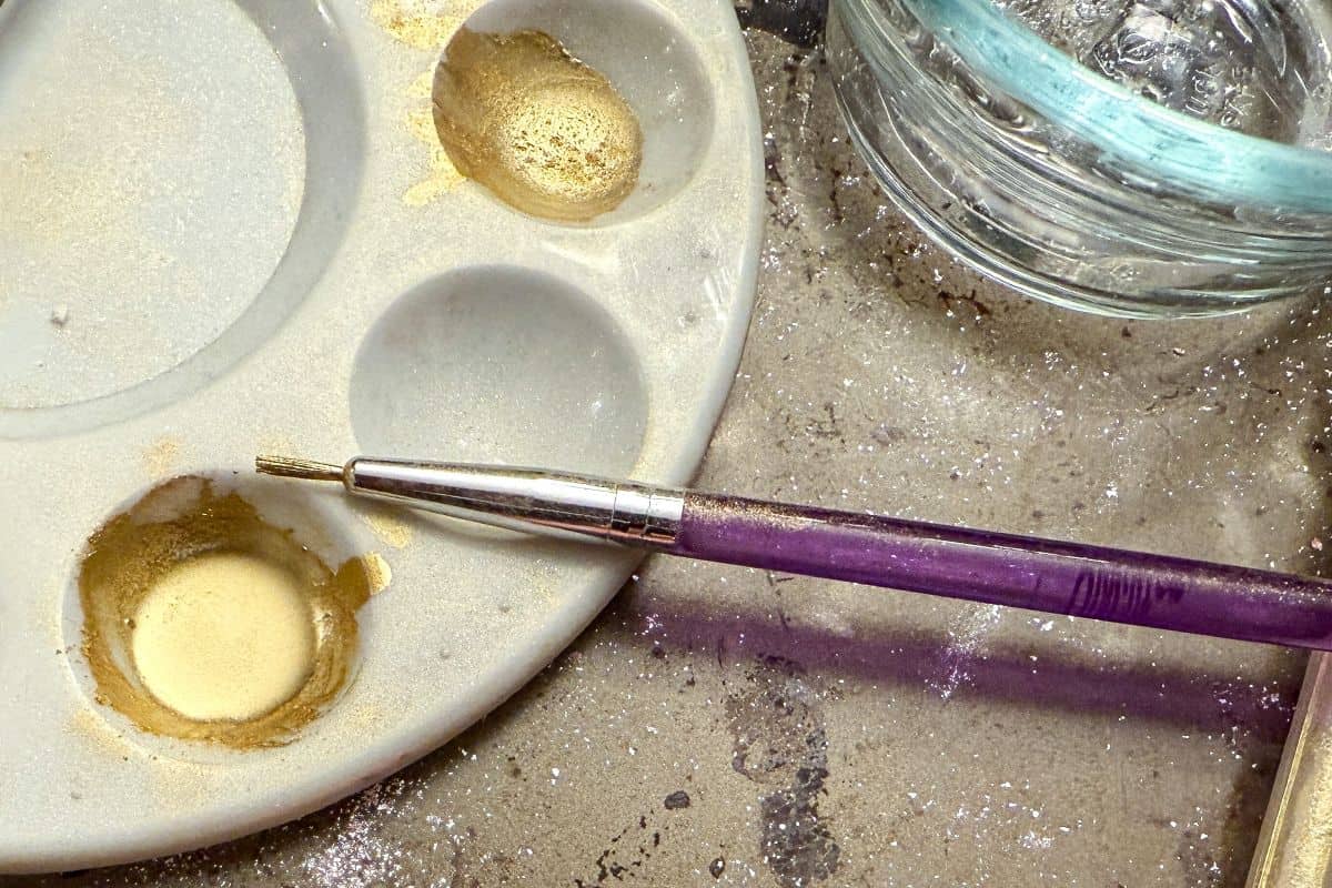 gold luster dust suspension in the well of a paint palette with a thin paintbrush