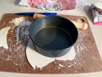a round cake pan on top of a thin piece of white rolled fondant