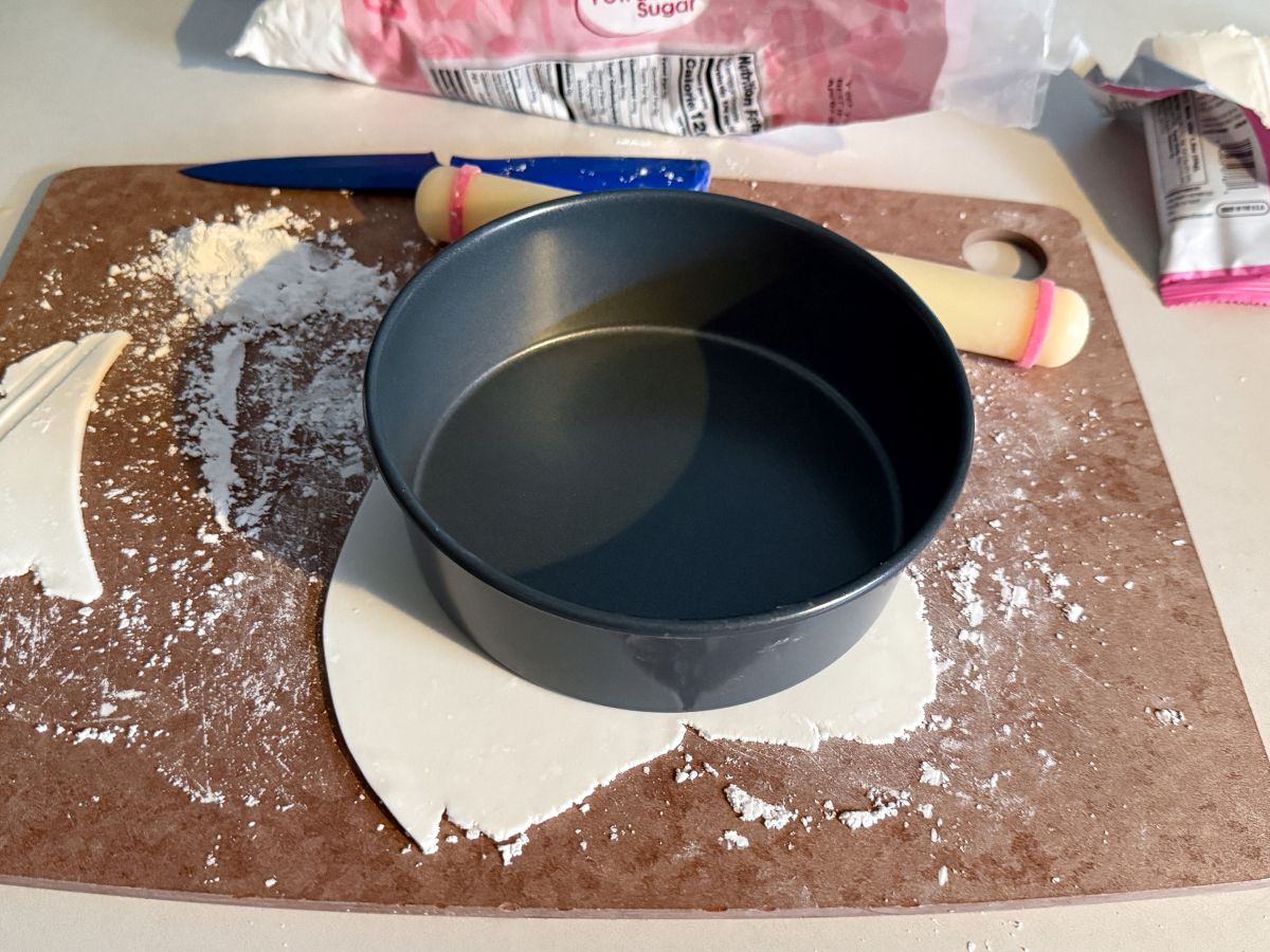 a round cake pan on top of a thin piece of white rolled fondant