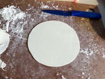 a white rolled fondant circle on a powdered sugar dusted cutting board with a paring knife