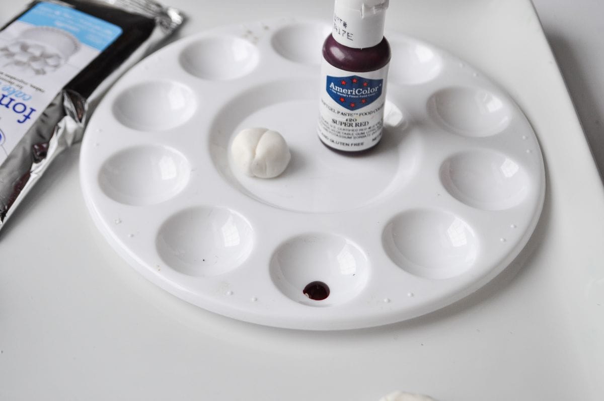white fondant shaped into a ladybug next to a bottle of red food coloring gel on a food dedicated paint palette