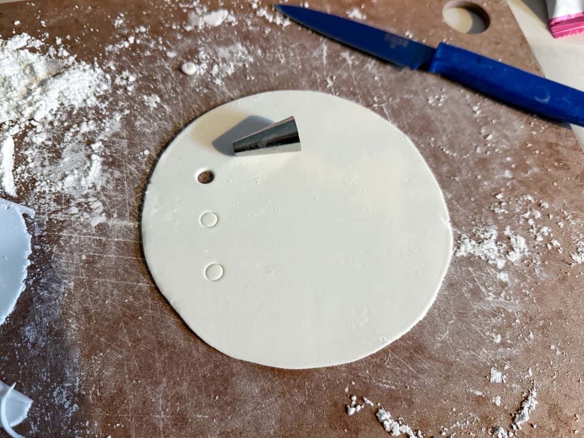 a round piece of rolled white fondant with a small circle punched out and markings for two more circles to be cut out