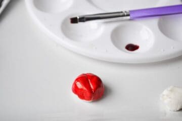 white fondant painted red with red food coloring gel next to a paint palette and food grade paintbrush