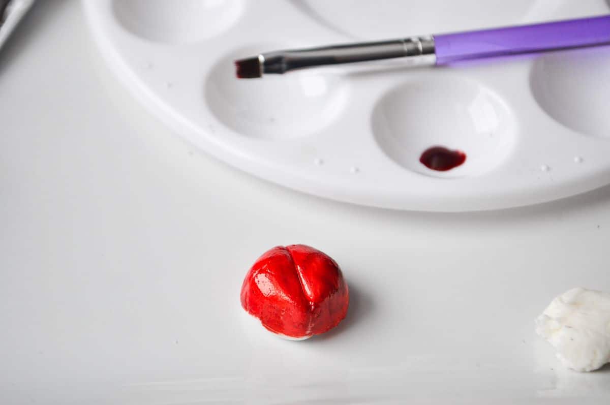 white fondant painted red with red food coloring gel next to a paint palette and food grade paintbrush