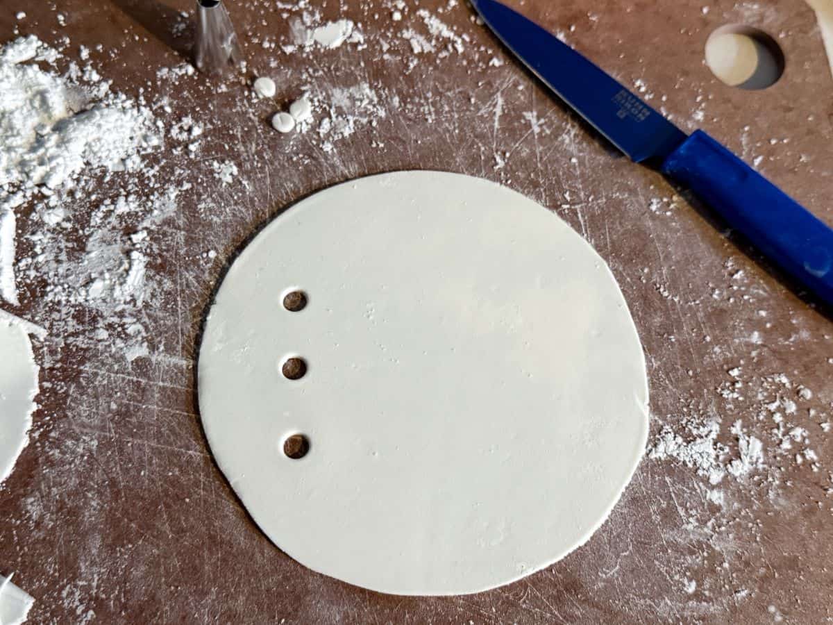 a round piece of white rolled fondant with 3 small circles cut down one side
