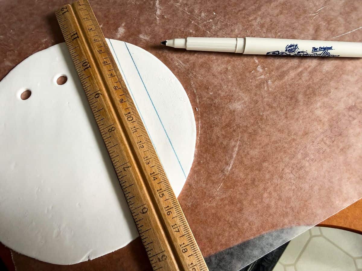 a wood ruler on top of a piece of a white rolled fondant circle with a blue line drawn with a blue food coloring marker
