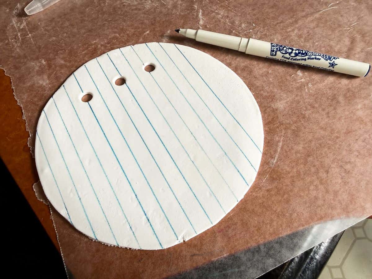 blue parallel lines drawn with a blue food coloring marker on a round piece of white rolled fondant