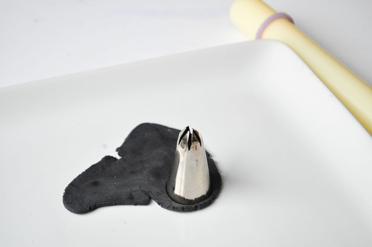 a large metal piping tip cutting out a circle of black fondant
