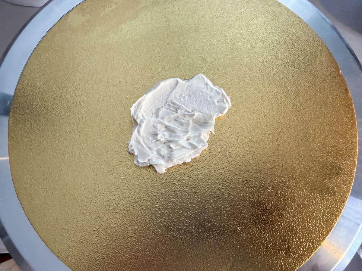 a gold round cake board with a smear of vanilla buttercream in the center