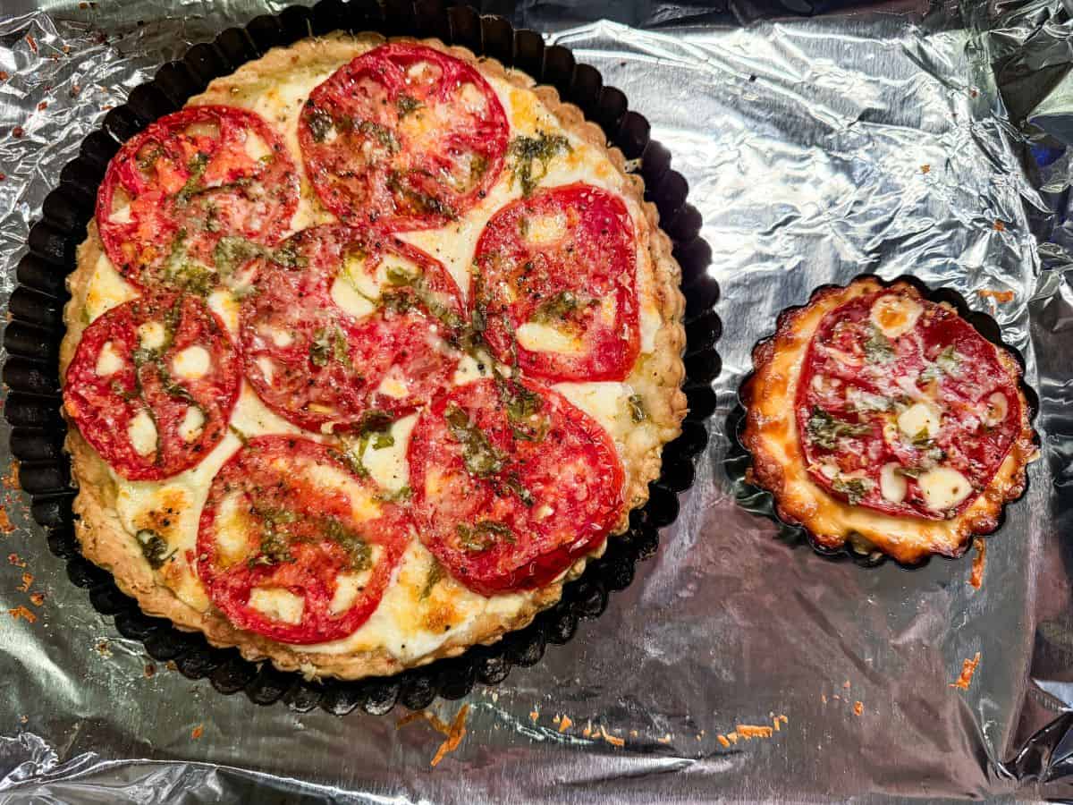a tomato mozzarella tart baked on foil lined pan next to a mini tartlet