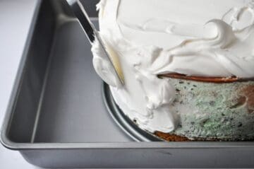 a metal offset spatula spreading whipped topping on an ice cream cake