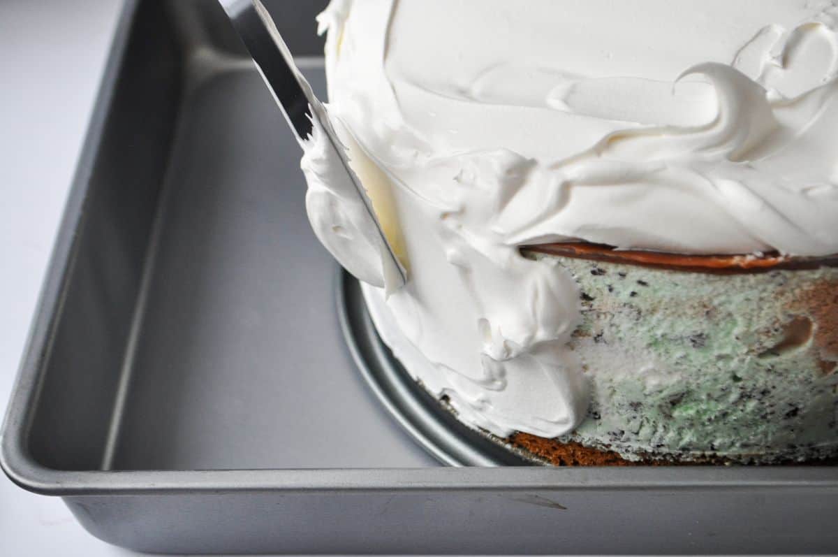 a metal offset spatula spreading whipped topping on an ice cream cake